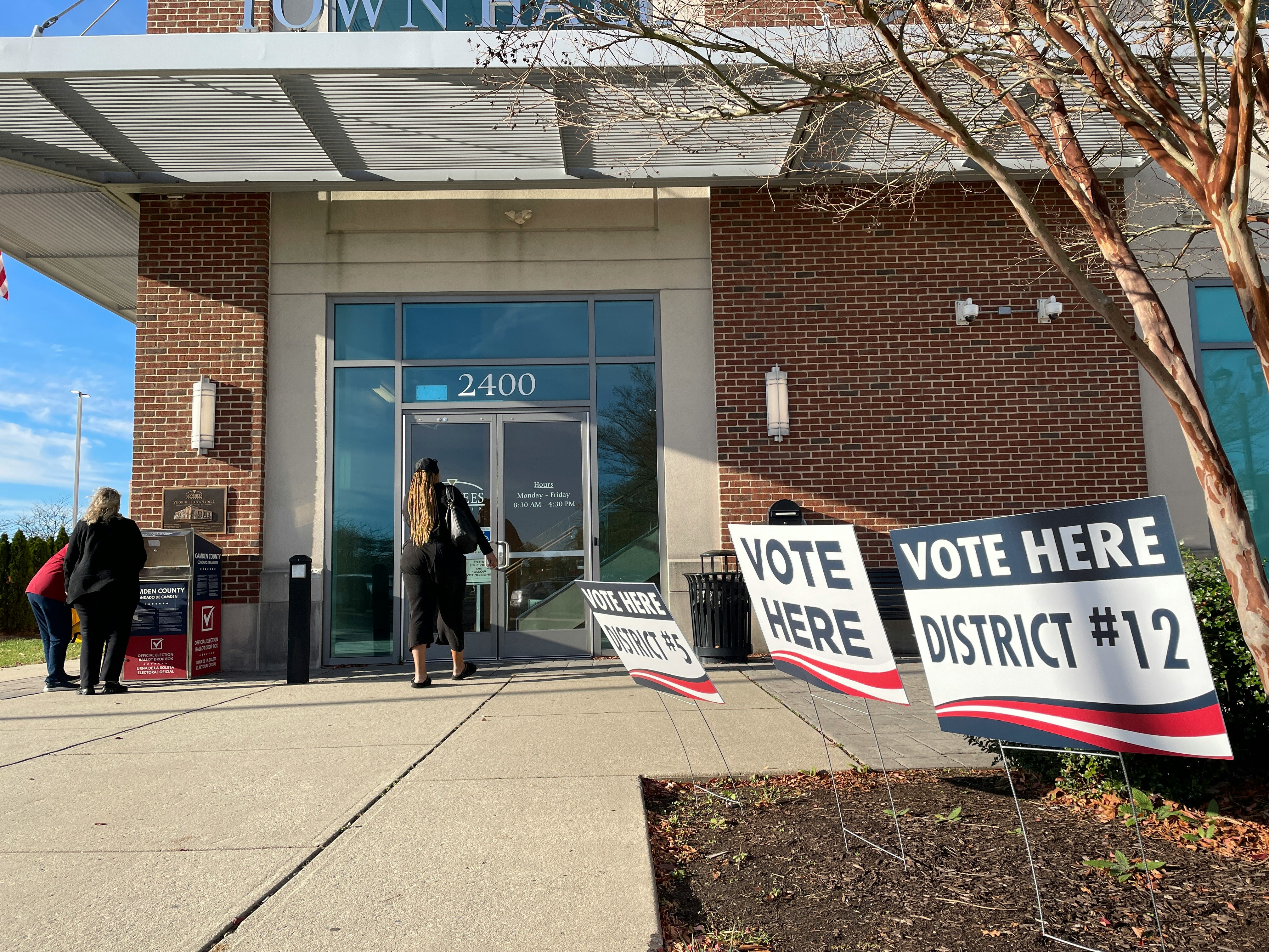 Voters walking up to a town hall polling place with 'Vote Here / District #12' signs out front.